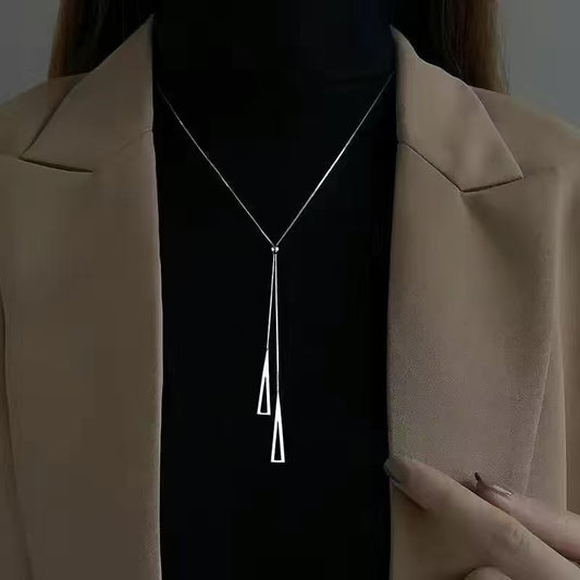 Person wearing a silver necklace with a pendant against a dark background