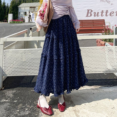 Person wearing a blue floral skirt with red shoes in an outdoor setting