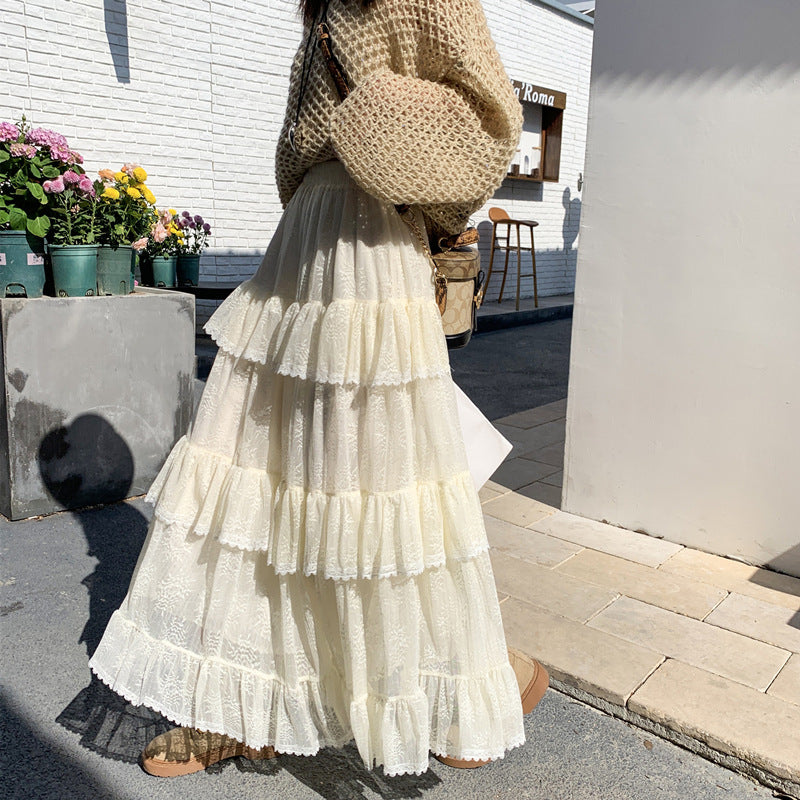 Person wearing a white tiered skirt and beige sweater standing outdoors.