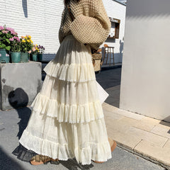 Person wearing a white tiered skirt and beige sweater standing outdoors.