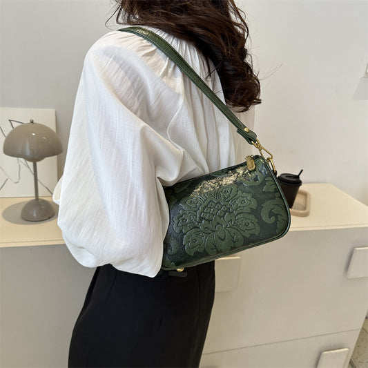 Person wearing a white shirt and holding a green handbag with floral patterns.