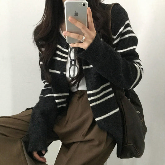 Person wearing a black and white striped cardigan with a plain background