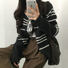 Person wearing a black and white striped cardigan with a plain background