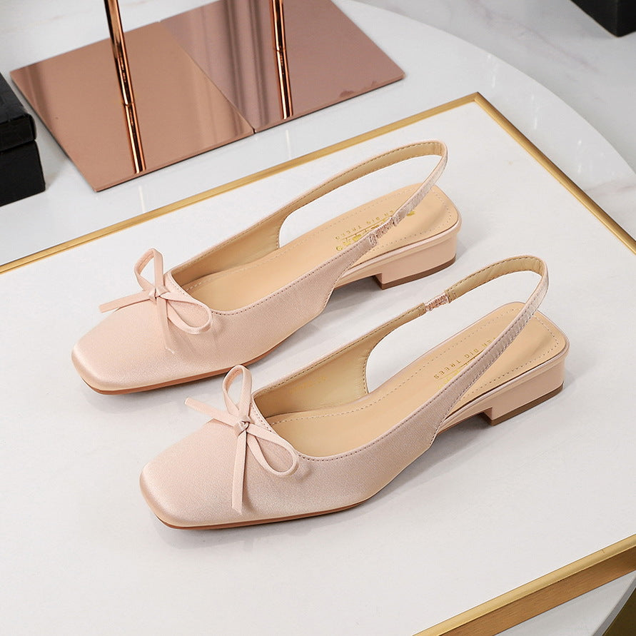 Pair of pink flat shoes with bow details on a white surface.