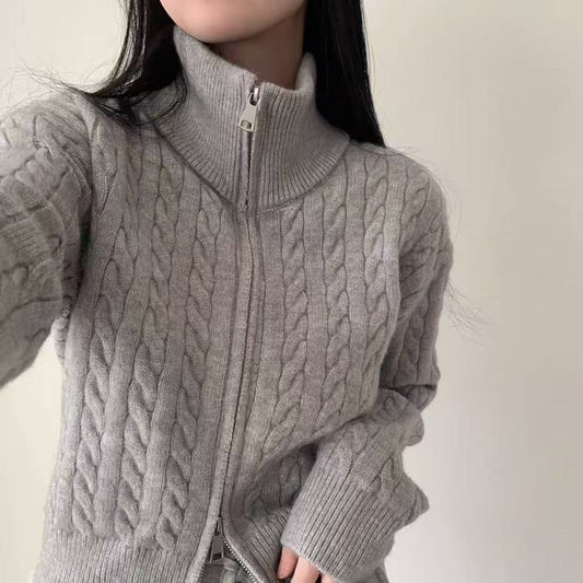 Person wearing a gray cable knit sweater with a zipper on a plain background