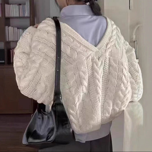 A person shown from the back wearing a cream cable-knit cropped sweater over a light blue collared shirt, with a black hair bow and a black shoulder bag in an indoor room setting.