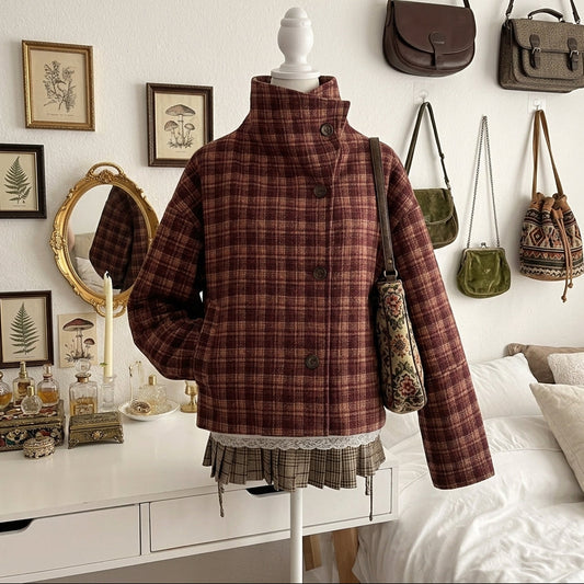 A brown and burgundy plaid high-neck jacket displayed on a mannequin in a styled bedroom setting, with a matching plaid pleated skirt and a patterned shoulder bag.