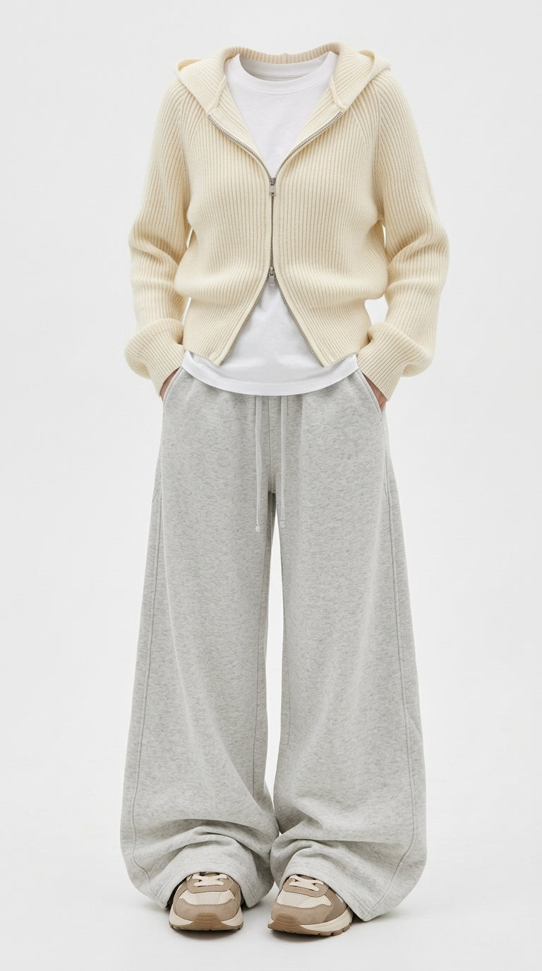 A model wearing a cream ribbed zip-up hooded cardigan over a white t-shirt, paired with light gray wide-leg sweatpants and beige sneakers, against a plain white studio background.