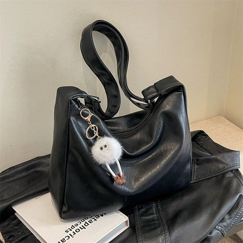 Black handbag with a fluffy keychain on a textured surface