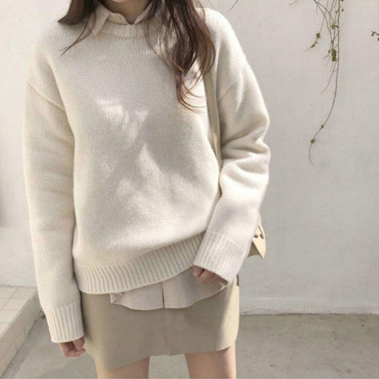 Person wearing a cream sweater over a light shirt with a beige skirt against a white background