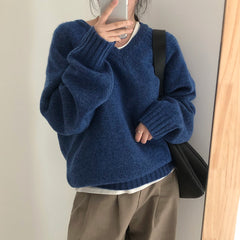 Person wearing a blue sweater and beige pants, holding a phone to take a mirror selfie.