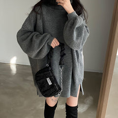 Person wearing a gray oversized sweater with a black bag in an indoor setting