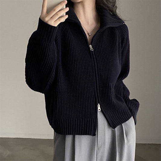 Person wearing a black zip-up sweater against a neutral background
