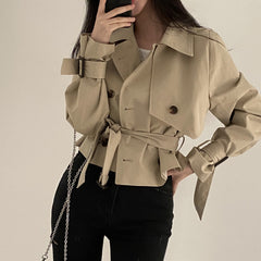 Person wearing a beige trench coat with a neutral background