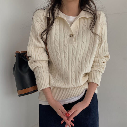 Person wearing a cream cable knit sweater with a plain background