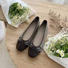 Pair of black shoes with a bow on a wooden surface surrounded by flowers