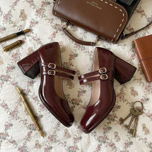 Brown patent leather shoes with buckles on a floral-patterned surface, surrounded by accessories.
