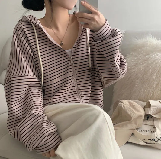 Person wearing a striped hoodie sitting on a couch with a neutral background