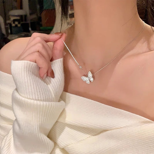 Butterfly necklace being worn by a person in a white outfit.