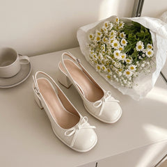 White shoes with bows on a table next to a bouquet of daisies and a cup.