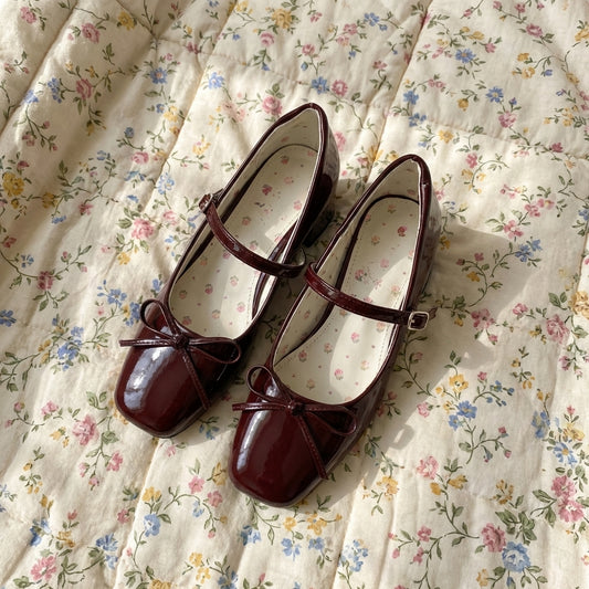 Pair of maroon shoes with bows on a floral fabric background