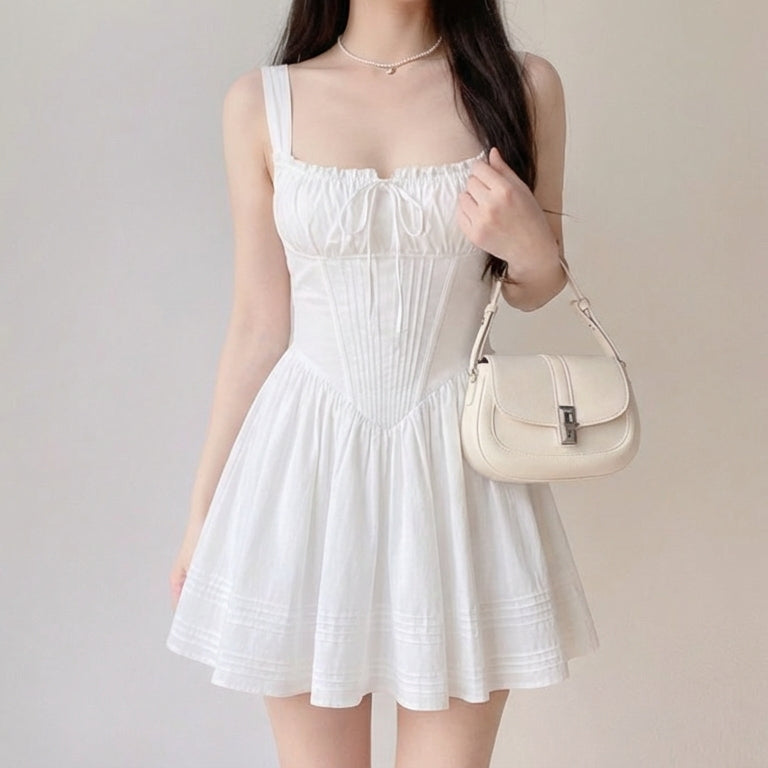 Woman wearing a white dress holding a beige handbag against a plain background