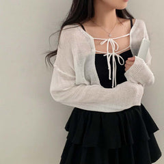 Person wearing a white cardigan over a black top and skirt against a plain background