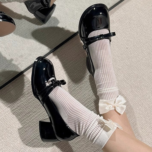 Black shoes with white socks featuring a bow on a neutral background