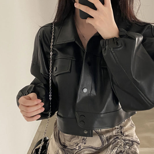 Person wearing a black leather jacket with a chain bag, holding a phone.
