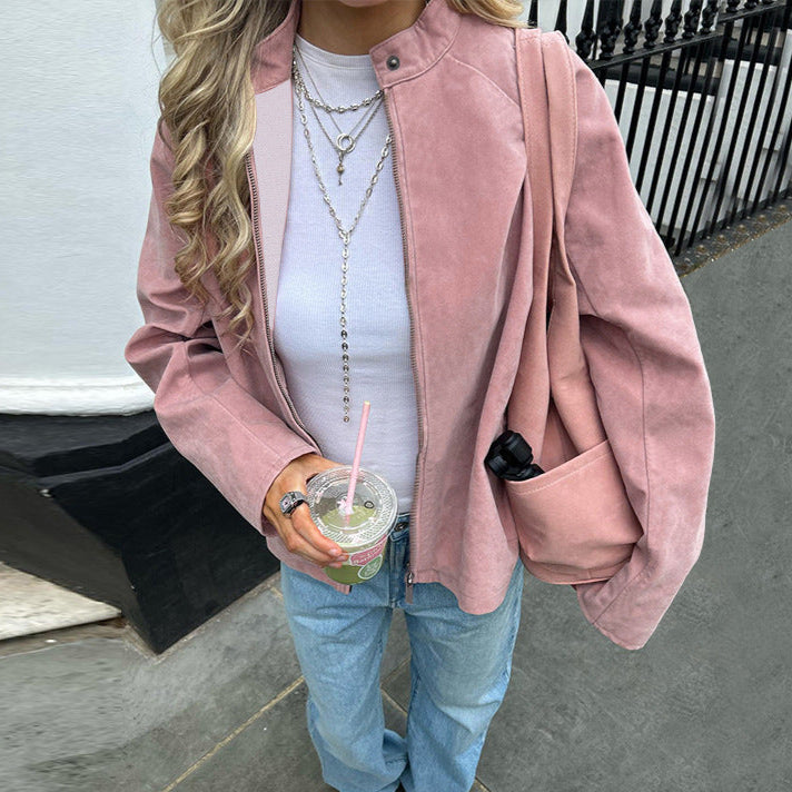 Person wearing a pink jacket over a white shirt and blue jeans, holding a drink.