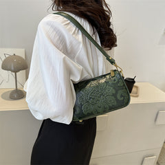 Person wearing a white shirt and holding a green handbag with floral patterns.