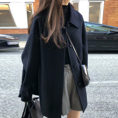 Person wearing a black coat and gray skirt on a street.