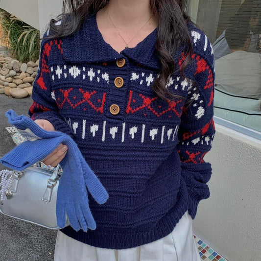 Person wearing a blue patterned sweater with red and white designs, holding blue gloves and a silver handbag.