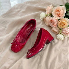 Red shoes with a bow on a beige surface next to a bouquet of flowers