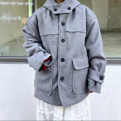 A young woman wearing a light gray oversized wool-blend coat with a high collar and large front pockets, standing in front of a storefront window.