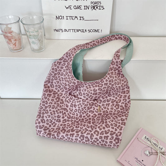A pink leopard-print shoulder bag with a mint green interior lining, styled on a white shelf next to two clear drinking glasses and a pink book.