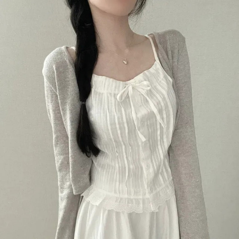 Woman wearing a white dress with a gray cardigan against a plain background