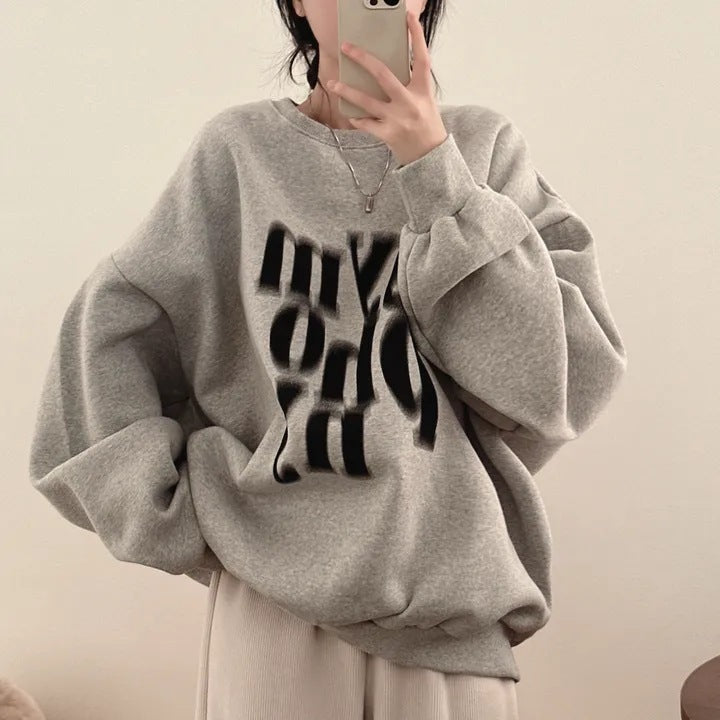 Person wearing a gray sweatshirt with black text, holding a phone.