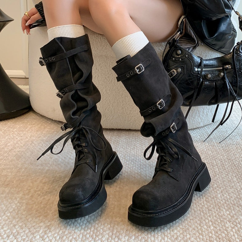 Black knee-high boots with buckles worn by a person sitting on a couch.