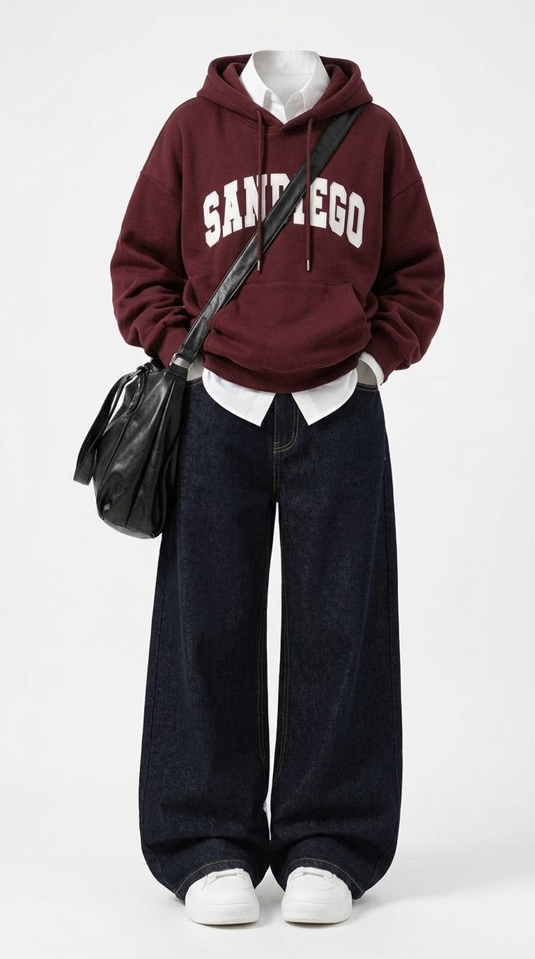 A mannequin styled with a maroon pullover hoodie featuring 'SAN DIEGO' in white varsity lettering, dark wide-leg denim jeans, a white collared shirt underneath, white sneakers, and a black shoulder bag, set against a plain white studio background.