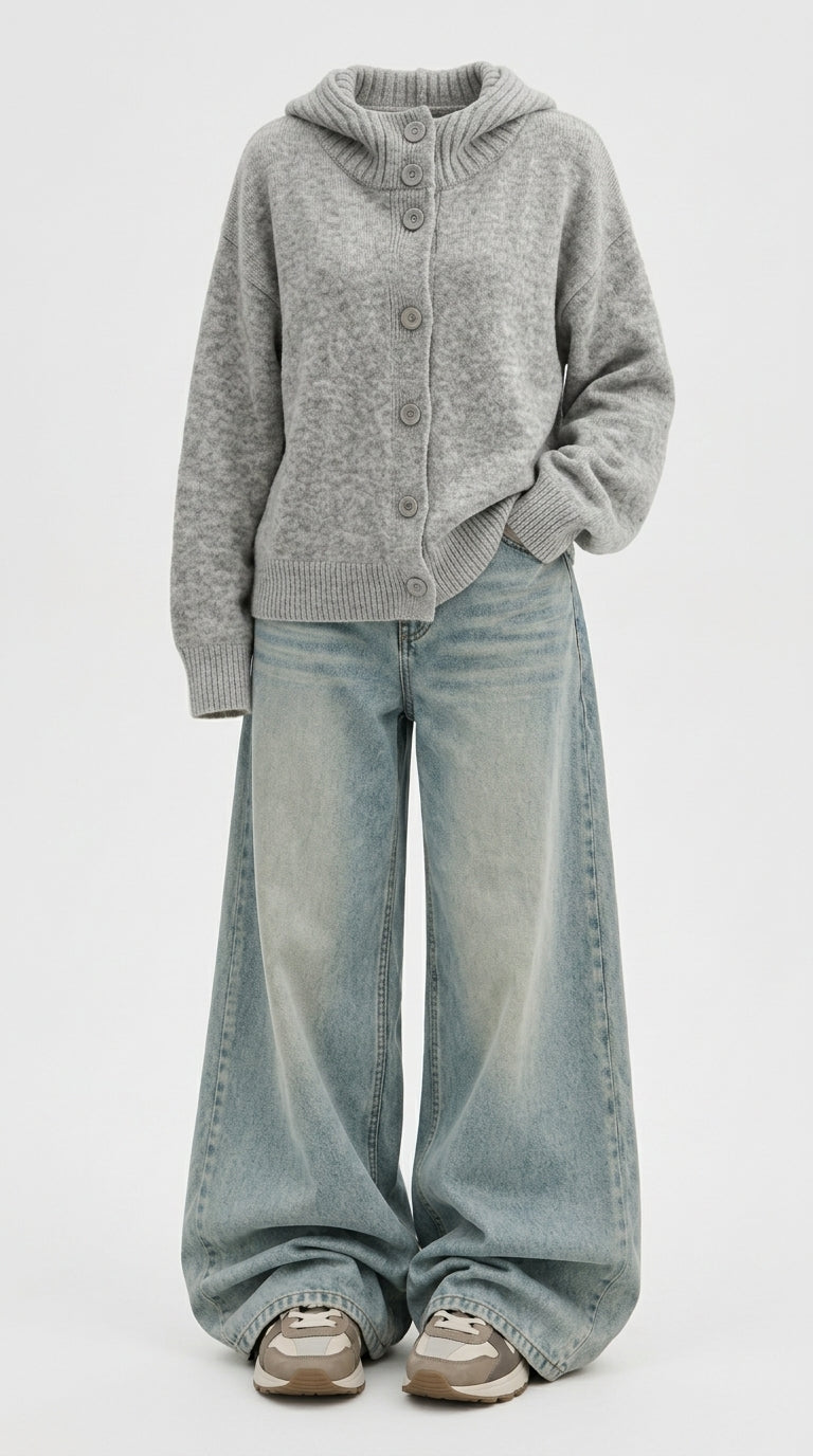 A person wearing a light gray knit button-front cardigan with a hood, paired with wide-leg light-wash blue jeans and beige sneakers, photographed against a plain light gray studio background.