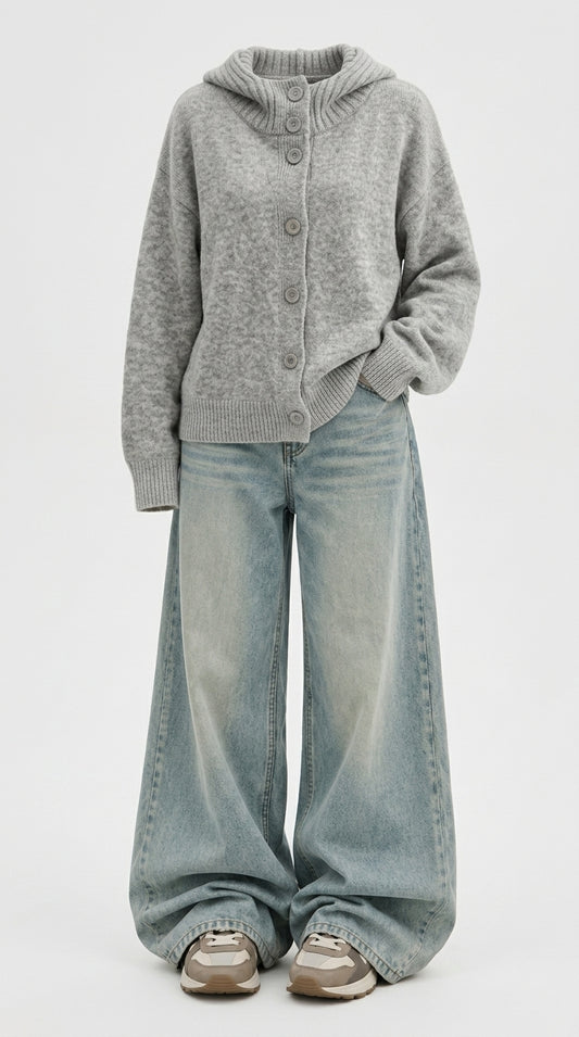 A person wearing a light gray knit button-front cardigan with a hood, paired with wide-leg light-wash blue jeans and beige sneakers, photographed against a plain light gray studio background.