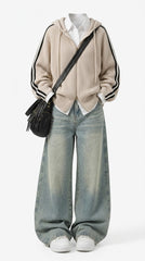 A full-body studio outfit on a mannequin or ghost form: a beige ribbed hooded zip cardigan with black-and-white striped sleeves over a white collared shirt, wide-leg light-wash blue jeans, white sneakers, and a black crossbody bag against a light gray background.