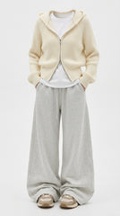 A model wearing a cream ribbed zip-up hooded cardigan over a white t-shirt, paired with light gray wide-leg sweatpants and beige sneakers, against a plain white studio background.