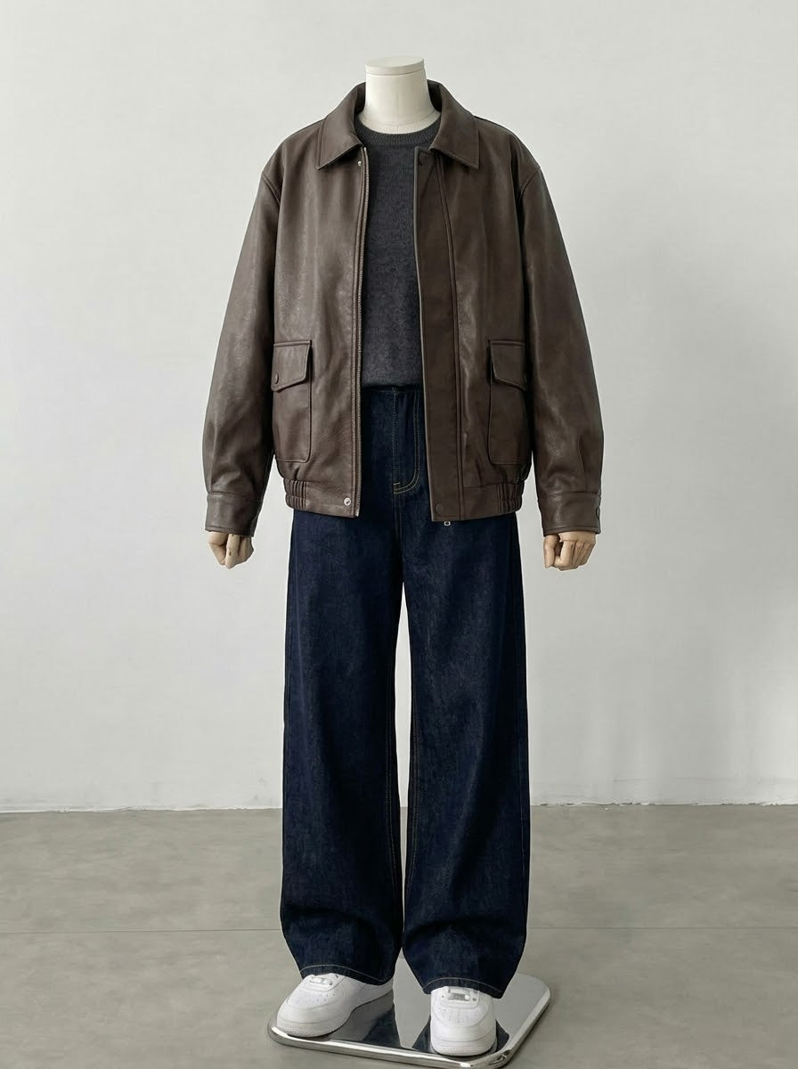 A mannequin wearing an oversized brown leather jacket over a dark gray turtleneck, paired with wide-leg dark blue jeans and white sneakers, set against a plain light gray studio background.