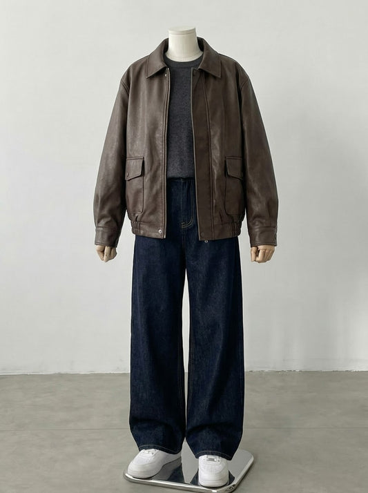 A mannequin wearing an oversized brown leather jacket over a dark gray turtleneck, paired with wide-leg dark blue jeans and white sneakers, set against a plain light gray studio background.