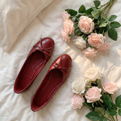 Red shoes with bows on a white surface with pink and white roses.