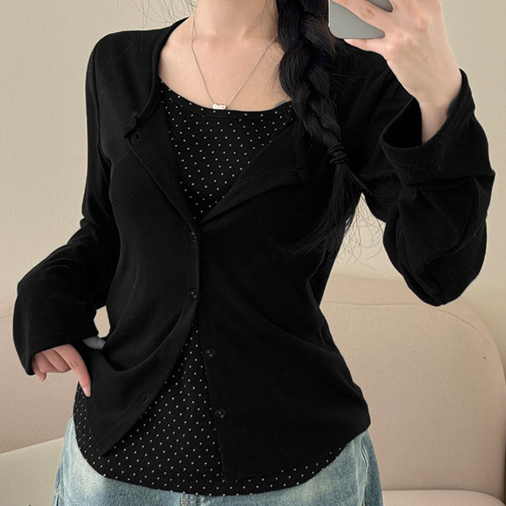 Person wearing a black blazer over a black polka dot shirt with a beige background