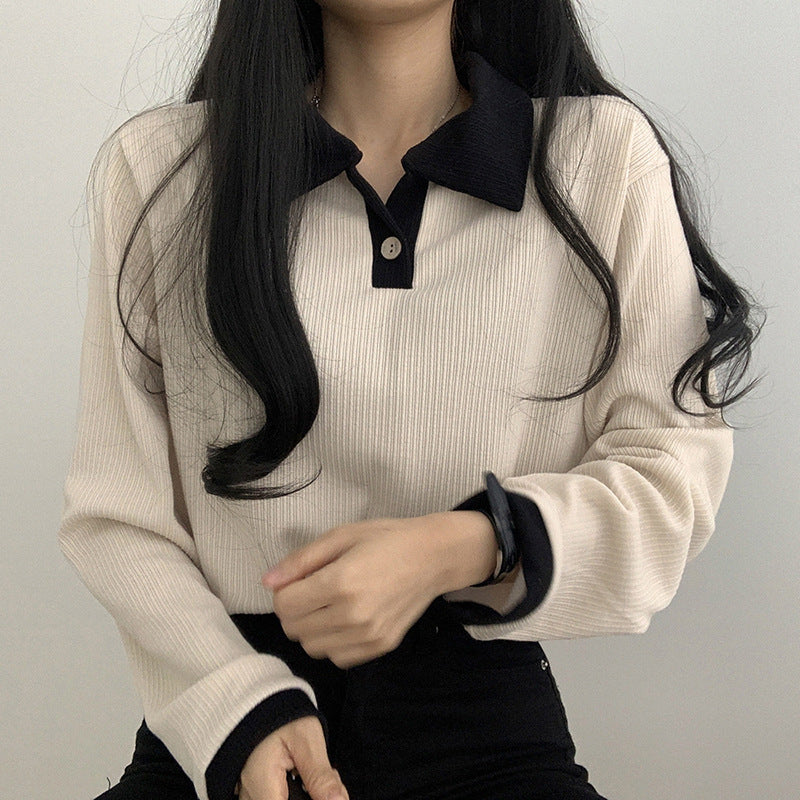 Person wearing a beige ribbed sweater with black collar and cuffs against a plain background