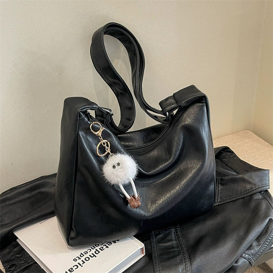 Black handbag with a fluffy keychain on a textured surface